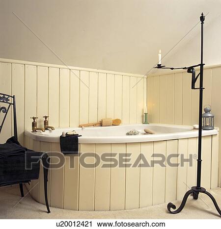 Stock Image - Traditional bathroom with cream painted panelling around corner bath with brass taps . Fotosearch