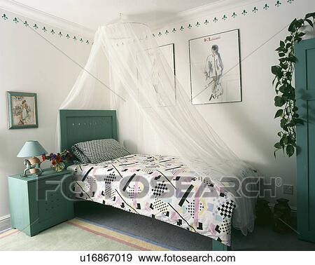 Stock Photo - Turquoise bedside cabinet and headboard in bedroom with abstract-patterned duvet and white mosquito net above the bed. Fotosearch