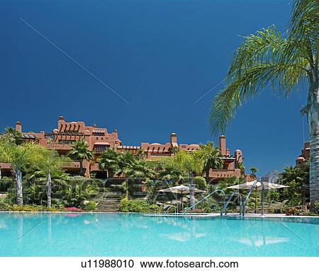 Stock Image - Turquoise swimmingpool in front of terracotta newbuild Spanish holiday village. Fotosearch