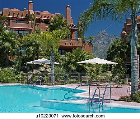 Stock Image - Turquoise swimmingpool with white parasols in front of newbuild apartment building in Spain. Fotosearch