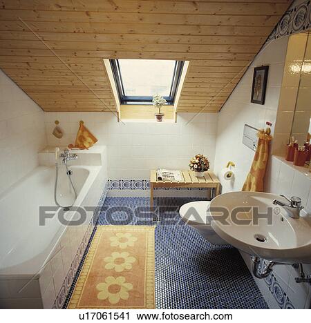 Stock Image - Velux window in wooden ceiling in attic bathroom with blue mosaic tiled floor and yellow floral bathmat. Fotosearch