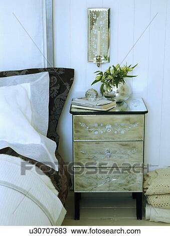 Venetian Glass Wall Sconce Above Glass Bedside Cabinet In Contemporary Bedroom Stock Image