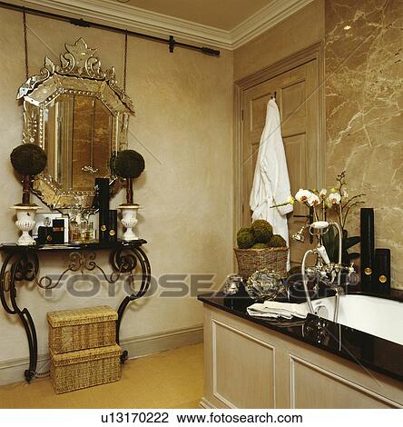 Ventian mirror above small topiary trees on metal console table in beige bathroom with marble wall above bath View Large Photo Image Stock Image - Ventian mirror above small topiary trees on metal console table in beige bathroom with marble wall above bath. Fotosearch