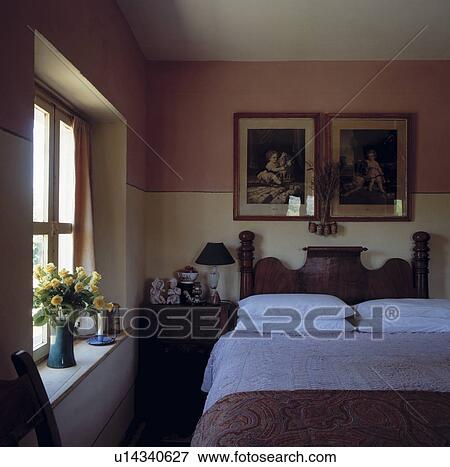 Victorian pictures above old mahogany bed with white pillows and bedcover in small bedroom with pink wall above dado View Large Photo Image Stock Photo - Victorian pictures above old mahogany bed with white pillows and bedcover in small bedroom with pink wall above dado. Fotosearch