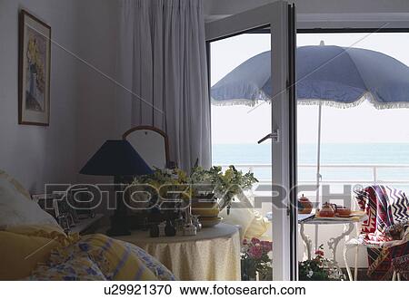 Stock Image - View from bedroom patio doors of parasol with table and chairs on balcony with view of the sea. Fotosearch