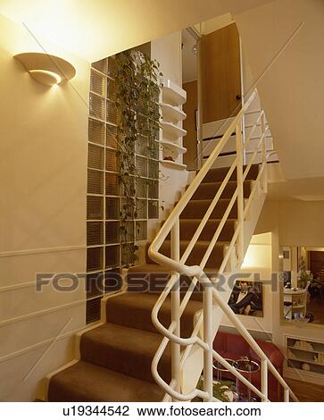 Stock Image - Wall-light and glass brick wall above staircase with brown carpet and white metal bannisters. Fotosearch