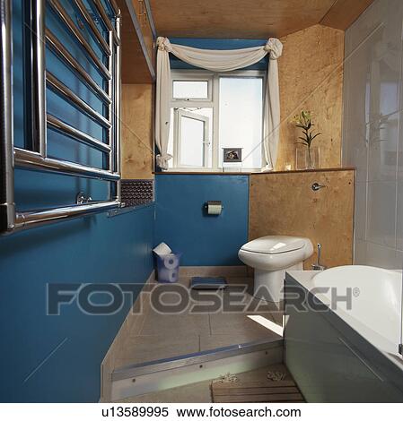 Wall-mounted steel radiator in split-level blue bathroom with toilet below walnut panelled wall View Large Photo Image Stock Photography - Wall-mounted steel radiator in split-level blue bathroom with toilet below walnut panelled wall. Fotosearch