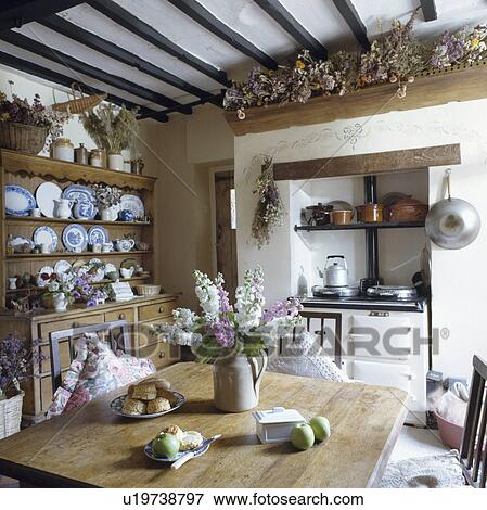 Stock Photo - White Aga oven in cottage kitchen with pine wood dresser and table with jug of pink and white flowers. Fotosearch