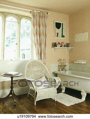 White cane armchair and antique table in front of window with in traditional bathroom with wooden flooring View Large Photo Image Picture - White cane armchair and antique table in front of window with in traditional bathroom with wooden flooring. Fotosearch