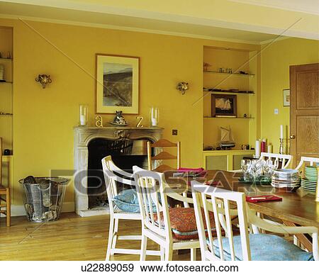 White chairs and wood table with crockery in yellow dining room with marble fireplace View Large Photo Image Stock Photo - White chairs and wood table with crockery in yellow dining room with marble fireplace . Fotosearch