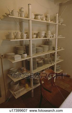 Stock Photo - White china jugs and plates on freestanding white metal shelf unit in dining room. Fotosearch