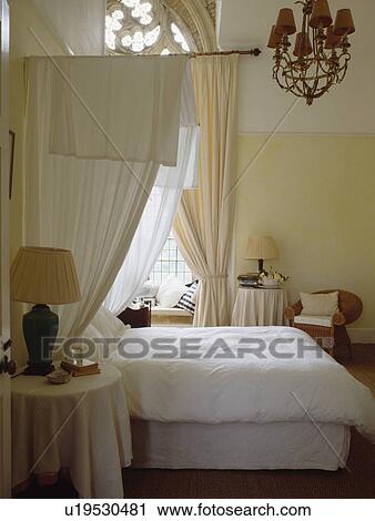 Stock Image - White curtains on half-tester bed in cream bedroom in converted church. Fotosearch