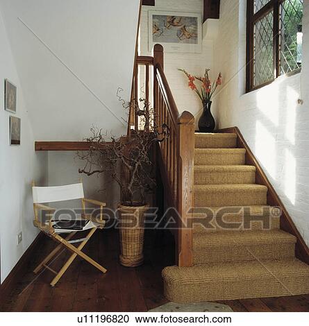 Stock Image - White director's chair and dried branches in basket beside wooden staircase with sisal carpet. Fotosearch