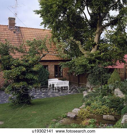 Stock Image - White furniture on patio in front of single-storey house. Fotosearch