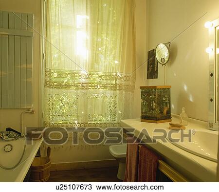 Stock Image - White lace curtains at window of traditional white bathroom. Fotosearch
