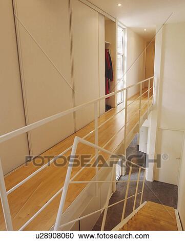 Stock Image - White metal bannisters on wooden landing walkway in modern white hall. Fotosearch