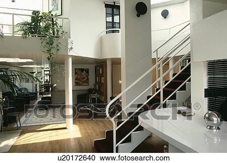 Stock Image - White metal staircase with black carpet in modern openplan loft conversion with wooden flooring. Fotosearch