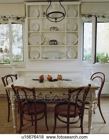 White plates on white shelves between windows in white dining room with bentwood chairs and old white table View Large Photo Image Stock Photo - White plates on white shelves between windows in white dining room with bentwood chairs and old white table. Fotosearch