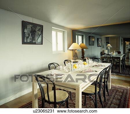 Stock Image - White rectangular table and black bentwood chairs in dining room with mirrored wall. Fotosearch