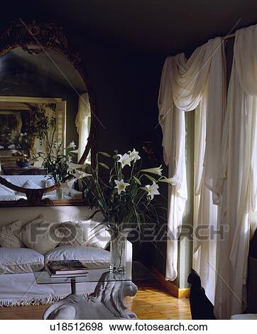 Stock Photo - White sofa and draped curtains in black living room. Fotosearch