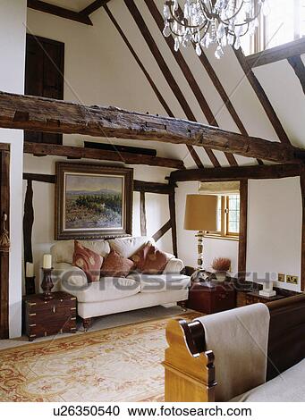 Stock Image - White sofa below large picture in country bedroom with beamed apex ceiling. Fotosearch