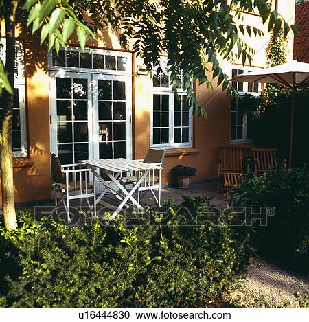Stock Image - White table and chairs on patio in front of traditional town house. Fotosearch