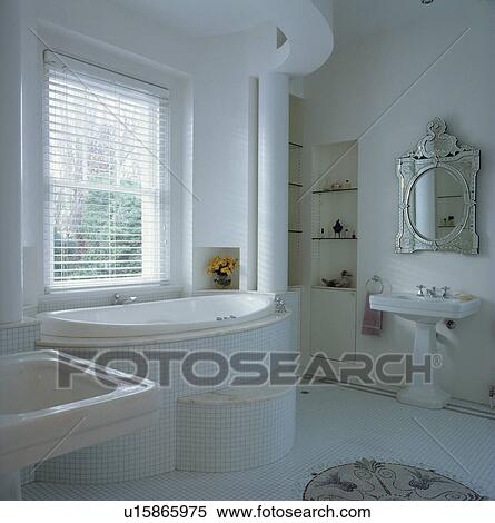 Stock Photography - White tiled architectural bathroom with bath on raised dais covered with mosaic tiles.. Fotosearch