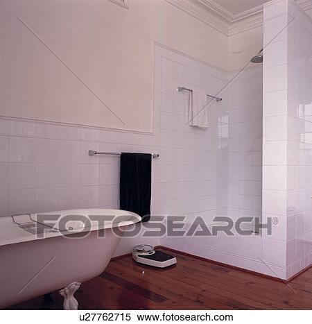 Stock Photography - White tiled bathroom with rolltop bath and shower with dado rail and cornice.. Fotosearch