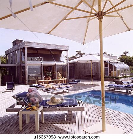 White umbrella above lounger on decking beside swimming pool in front of modern wooden house on the coast View Large Photo Image Stock Photo - White umbrella above lounger on decking beside swimming pool in front of modern wooden house on the coast. Fotosearch