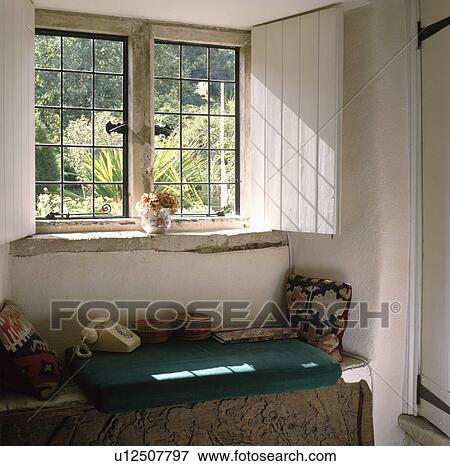 Stock Photo - White wooden shutters at cottage casement window above windowseat with telephone and patterned cushions. Fotosearch