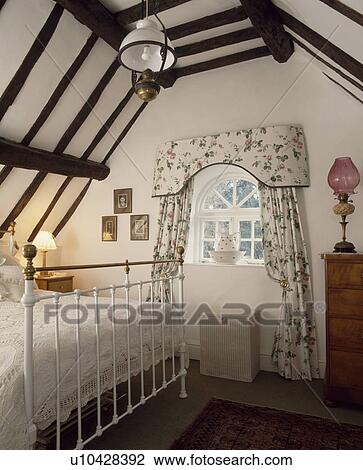 White wrought-iron bed in country bedroom with floral patterned curtains and pelmet at small arched window View Large Photo Image Stock Image - White wrought-iron bed in country bedroom with floral patterned curtains and pelmet at small arched window. Fotosearch