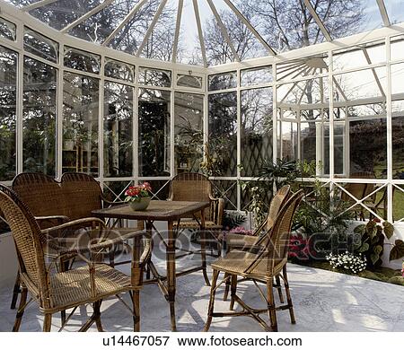 Stock Photo - Wicker chairs and table in glass conservatory dining room. Fotosearch