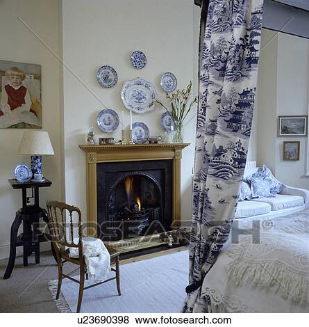 Willow-pattern drapes on four-poster bed in traditional bedroom with blue+white plates on wall above pine fireplace View Large Photo Image Stock Photo - Willow-pattern drapes on four-poster bed in traditional bedroom with blue+white plates on wall above pine fireplace. Fotosearch