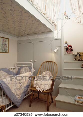 Stock Photography - Windsor chair beside white cot in child's bedroom with grey wooden staircase to mezzanine. Fotosearch