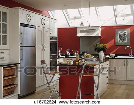 Wood and metal stools at breakfast bar in red kitchen with white fitted cupboards and tall fridge freezer View Large Photo Image Picture - Wood and metal stools at breakfast bar in red kitchen with white fitted cupboards and tall fridge freezer. Fotosearch