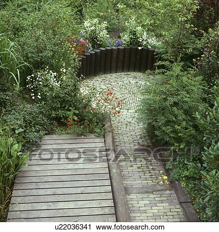 Stock Image - Wooden decking path to sunken circular paved patio in country garden in summer . Fotosearch