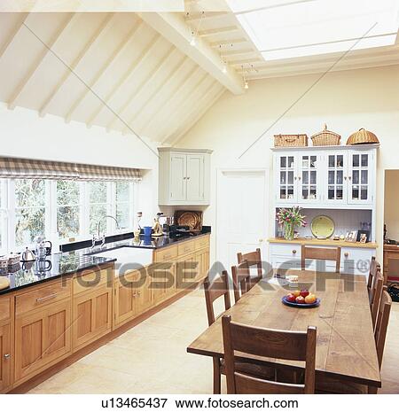 Stock Photo - Wooden dining table and chairs in cream kitchen extension with wooden units. Fotosearch