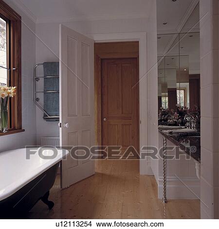 Picture - Wooden flooring and rolltop bath in modern white bathroom with door open to landing. Fotosearch