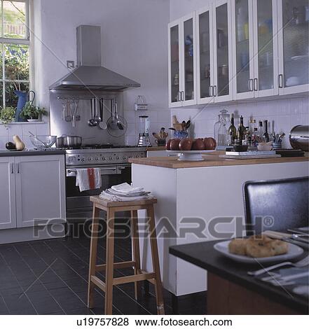 Wooden stool by counter in modern white kitchen with range oven View Large Photo Image Stock Photo - Wooden stool by counter in modern white kitchen with range oven . Fotosearch