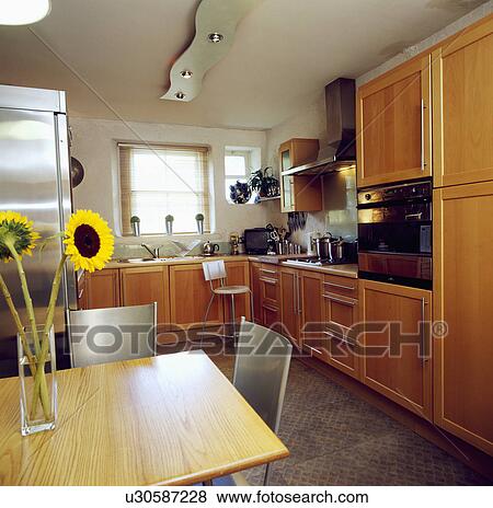 Stock Photo - Wooden table and metal chairs in modern pale wood kitchen. Fotosearch