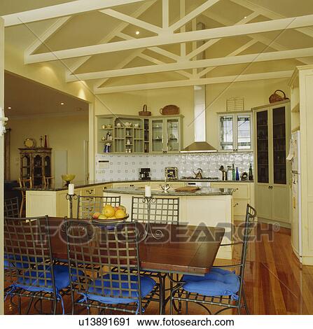 Wooden table and metal chairs with blue cushions in modern cream kitchen dining room with apex ceiling View Large Photo Image Stock Image - Wooden table and metal chairs with blue cushions in modern cream kitchen dining room with apex ceiling. Fotosearch