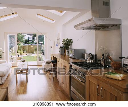 Stock Image - wooden units & flooring in modern kitchen & livingroom extension with view of the garden through open glass doors. Fotosearch