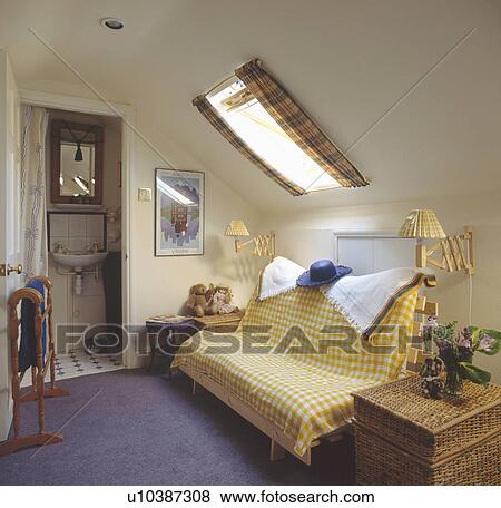 Stock Photo - Yellow & white checked throw on futon sofabed in attic bed sitting room with door open to ensuite bathroom. Fotosearch