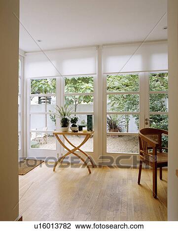 光景 の 中庭 ガラスを通って ドア で 白 ﾌﾞﾗｲﾝﾄﾞ 中に 現代 Livingroom で 小さい テーブル 上に 木製の床 ストックイメージ U Fotosearch