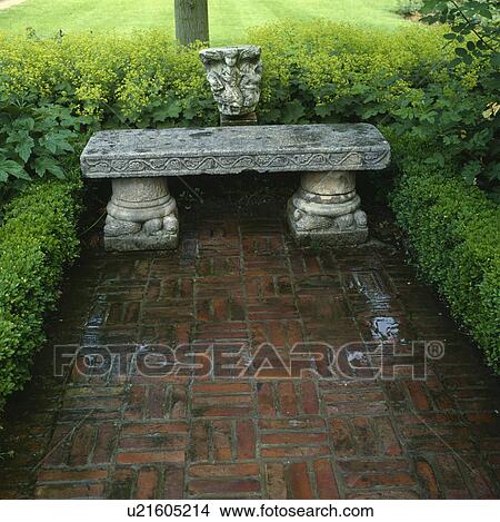 Picture - &#13; &#10; Carved stone seat on brick block paving as a feature in a large country garden. Fotosearch
