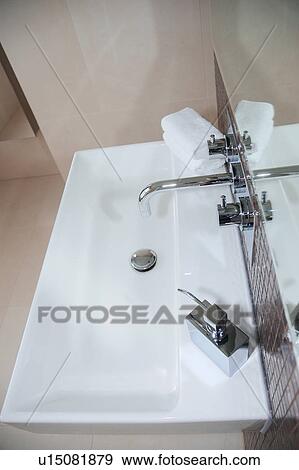 Stock Photo - Aerial view of stainless steel tap and soap dispenser above rectangular white ceramic basin. Fotosearch