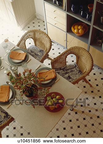Aerial view of wicker chairs and table with orange napkins on plates in dining room with black and white tiled floor View Large Photo Image Stock Photograph - Aerial view of wicker chairs and table with orange napkins on plates in dining room with black and white tiled floor. Fotosearch