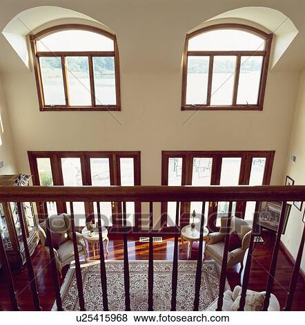 Stock Photo - Aerial view over wooden banisters to double height modern livingroom . Fotosearch