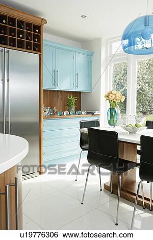 Stock Photograph - American-style stainless steel fridge freezer in modern white kitchen with white flooring and pale turquoise cupboards. Fotosearch