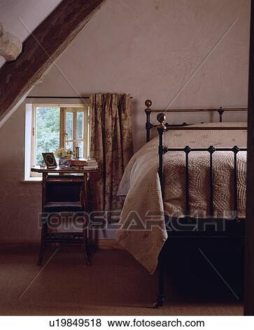 Stock Photo - Antique brass and iron bed in cottage attic bedroom with floral curtains and quilt. Fotosearch